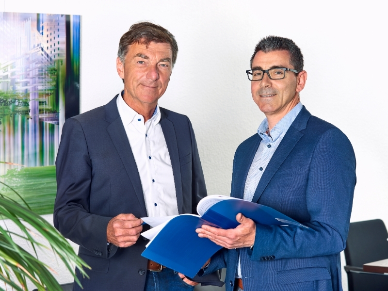 Herr Wolvers und Herr Neuy mit Arbeitsmappe.